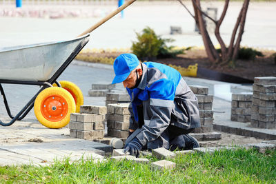 Bricklayer in work clothes sits on sidewalk and lays out paving slabs. sight of working man in open