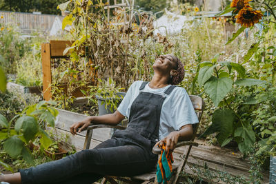 Happy female agricultural shareholder relaxing on chair in urban garden