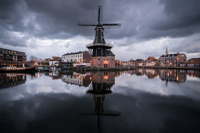 Reflection of traditional windmill on river in city at dusk