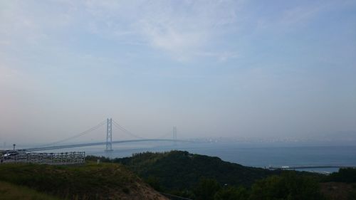 Suspension bridge over water against cloudy sky