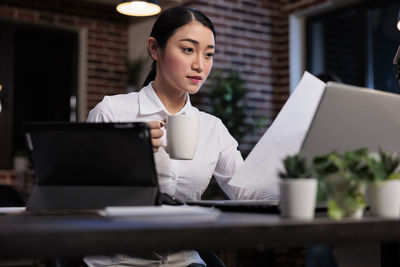 Businesswoman reading document while holding coffee cup