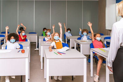 Cute kids wearing mask raising hands at hospital