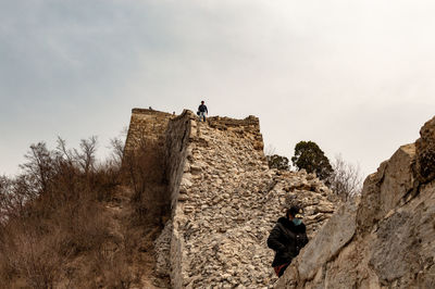 Low angle view of men standing on rock against sky