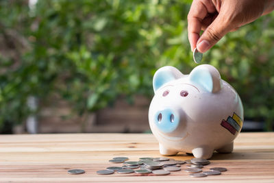 Close-up of hand inserting coin in piggy bank on table