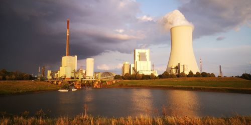 Factory by river against sky