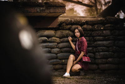 Portrait of young woman sitting against wall