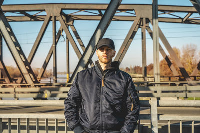 Portrait of man standing against bridge in city during winter