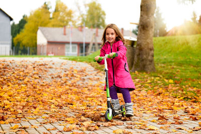 Portrait of girl riding push scooter at park during autumn