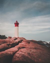 Lighthouse on rock by building against sky