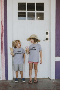 Happy siblings with ice cream looking at each other while standing against door