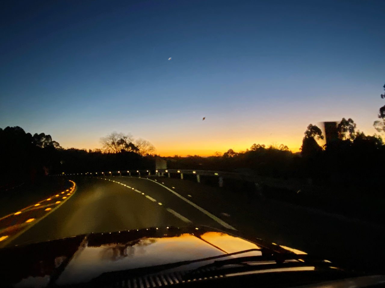 ROAD SEEN THROUGH CAR WINDSHIELD DURING SUNSET