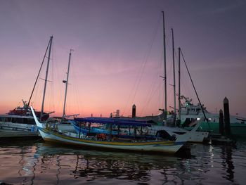 Sailboats moored in harbor at sunset