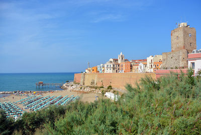 Buildings by sea against blue sky