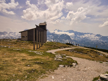 Building on field by mountain against sky