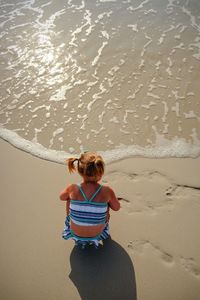 High angle view of girl crouching on shore at beach