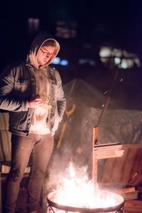 Young man standing by fire pit at night