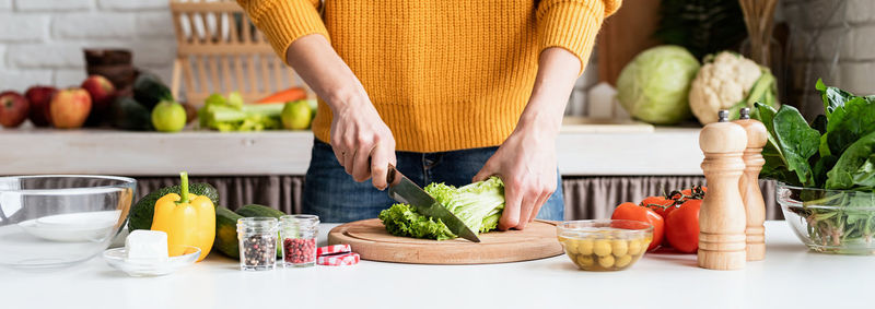 Healthy eating. woman in yellow sweater preparing greek salad in kitchen. banner. front view