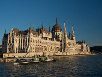 View of buildings by river against clear blue sky