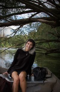 Portrait of smiling young woman by lake at park