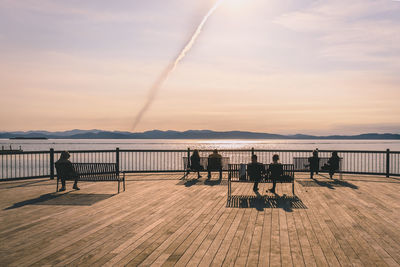 People sitting on bench promenade at against river