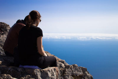Rear view of woman sitting on rock looking at sea