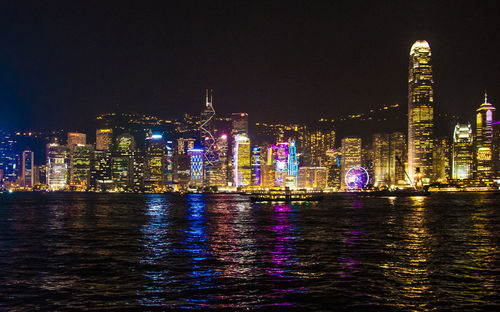 Illuminated cityscape by sea against sky