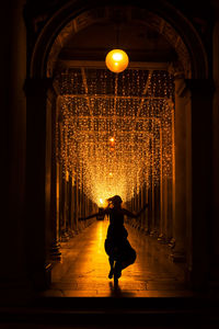 Rear view of woman walking in illuminated corridor