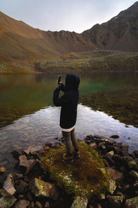 Travel photographer taking pictures of nature on a smartphone, mountain landscape by the lake person