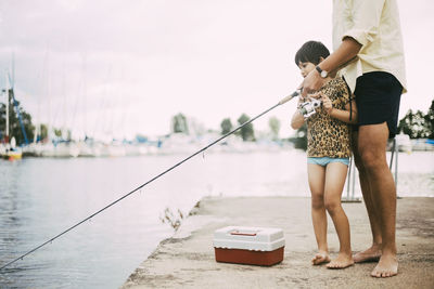 Low section of father and daughter fishing in lake during summer