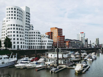 Boats moored at harbor by buildings against sky