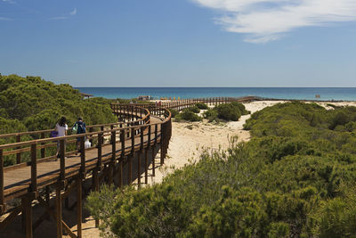 Friends walking on pier at beach against blue sky