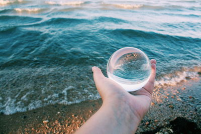 Midsection of person holding sunglasses at beach