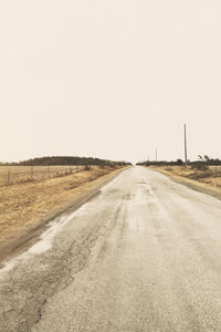 Road amidst field against clear sky