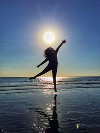 Silhouette woman jumping over shore at beach against sky