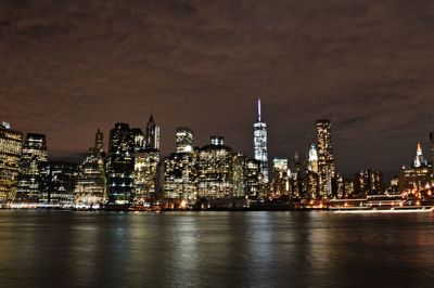 Illuminated buildings by river against sky at night