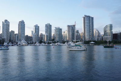 Sailboats in city by sea against sky
