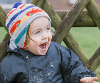 Close-up of cute happy girl with mouth open standing against fence