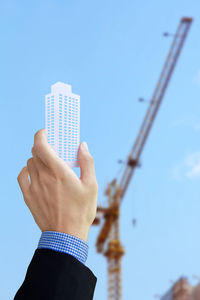 Close-up of hand holding construction site against clear blue sky