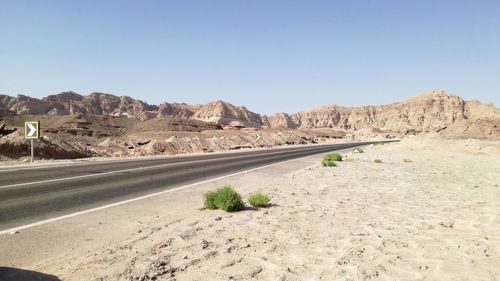 Road leading towards mountains against clear sky