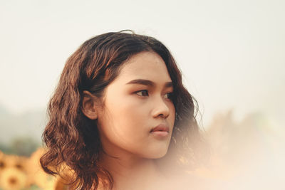 Close-up of thoughtful young woman standing at sunflower farm against clear sky