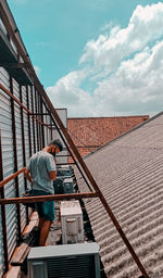 Side view of man working on railing against sky