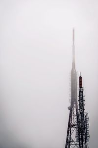 Low angle view of communication towers against sky during foggy weather