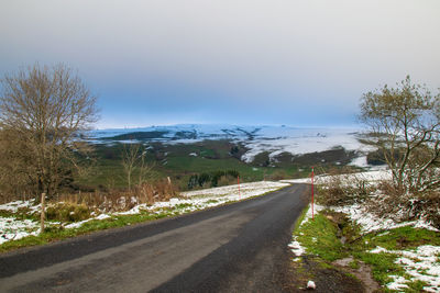 Road by trees against sky during winter