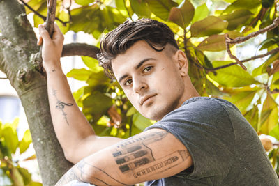 Portrait of young man sitting on tree