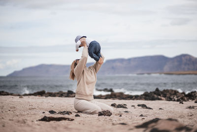 Full length of young woman exercising at beach against sky