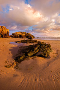 Rock formation on beach against sky during sunset