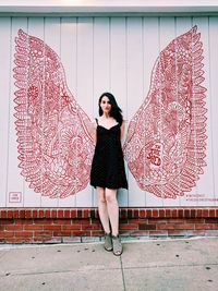 Full length portrait of woman standing against wall