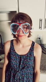 Portrait of young woman wearing swimming goggles while standing at home