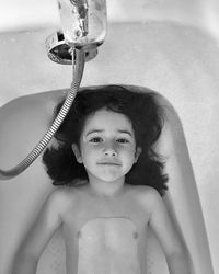 High angle portrait of cute shirtless girl lying in bathtub at bathroom