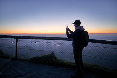 Full length of man photographing sea against sky during sunset